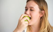 Young female dental patient, eating an apple and satisfied with her recent dental procedure.